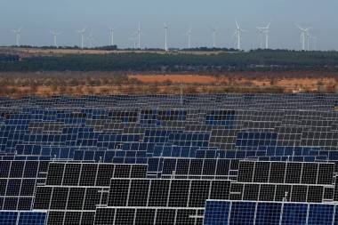 Photovoltaic power panels stand at Abaste's El Bonillo Solar Plant while wind turbines spin at a wind farm on the background in El Bonillo, Albacete province, Spain.