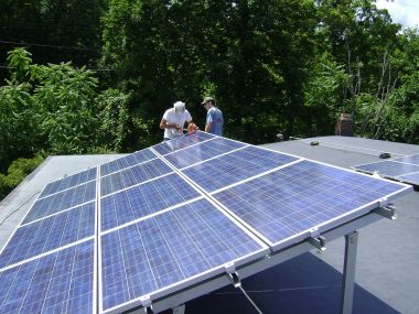 Two workers installing a tilt-up PV array on a roof near Poughkeepsie, NY. Photo by Lucas Braun. CC BY-SA 3.0 unported. Wikimedia Commons.